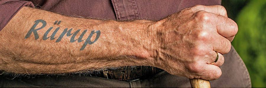 Rürup-Rente – Tattoo auf Unterarm eines alten Mannes, Faust hält Wanderstock